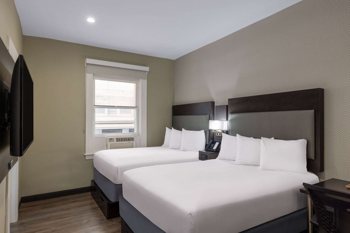 A hotel room with two beds, a TV, a window, and a desk.