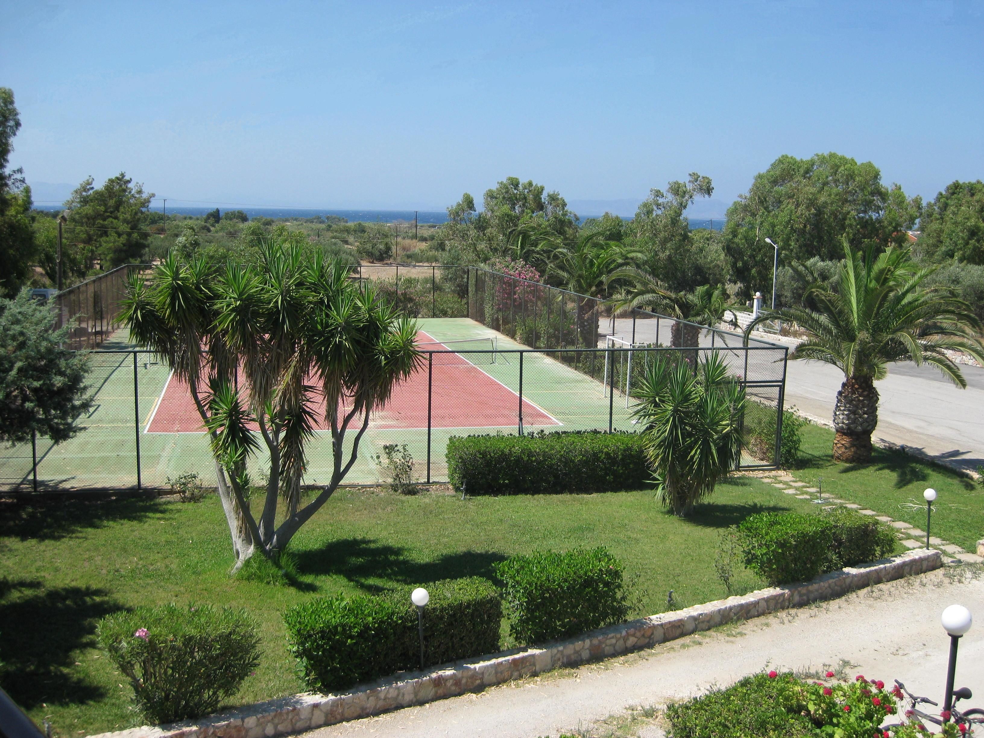Una cancha de tenis rodeada de vegetación y vistas despejadas al mar.
