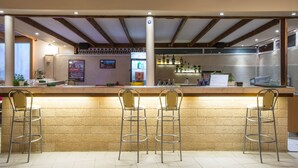 Un espace bar avec trois tabourets de bar en métal, un comptoir avec un menu et une cuisine en arrière-plan.