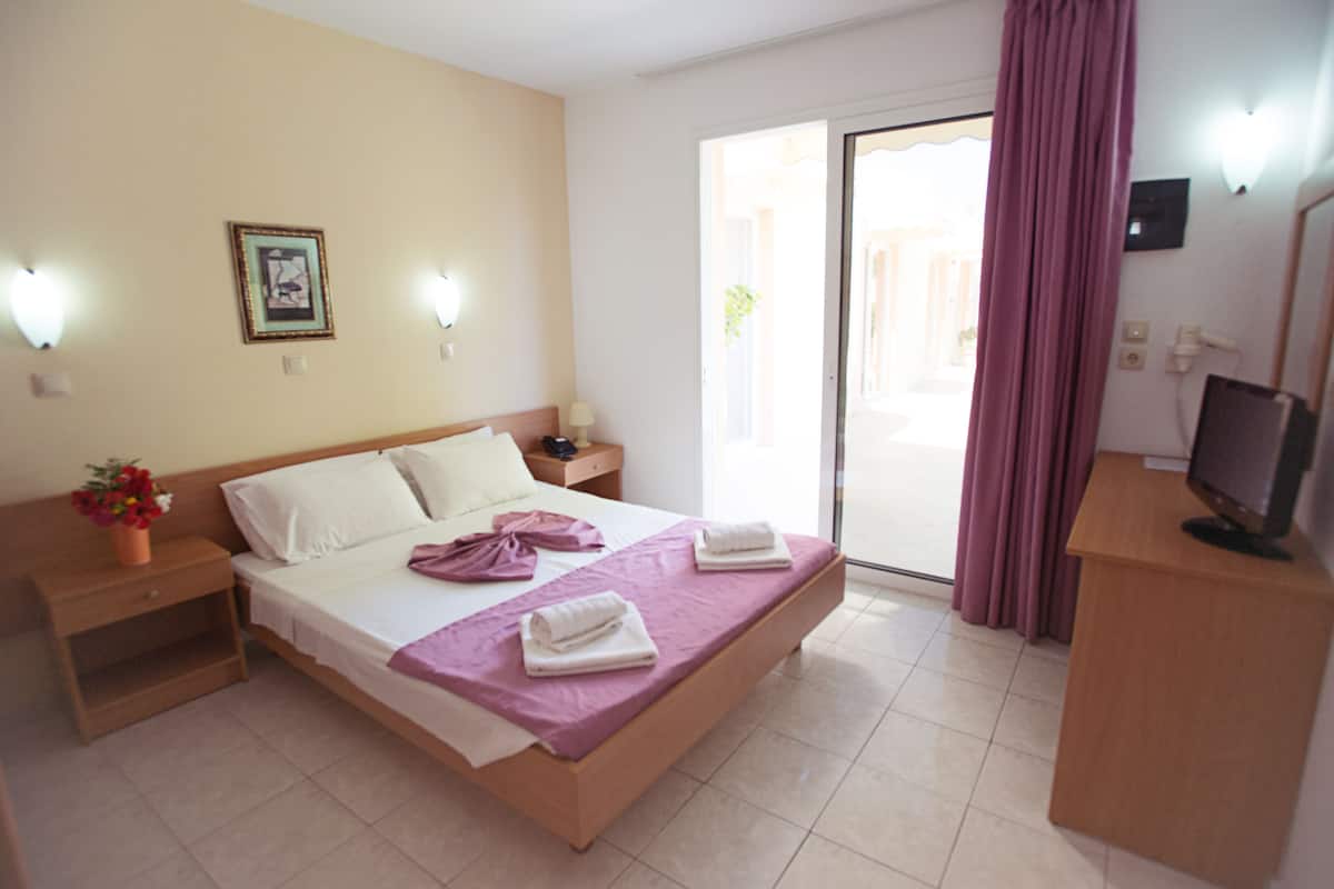 Habitación de hotel con cama, mesita de noche, escritorio con computadora y ventana con cortinas.