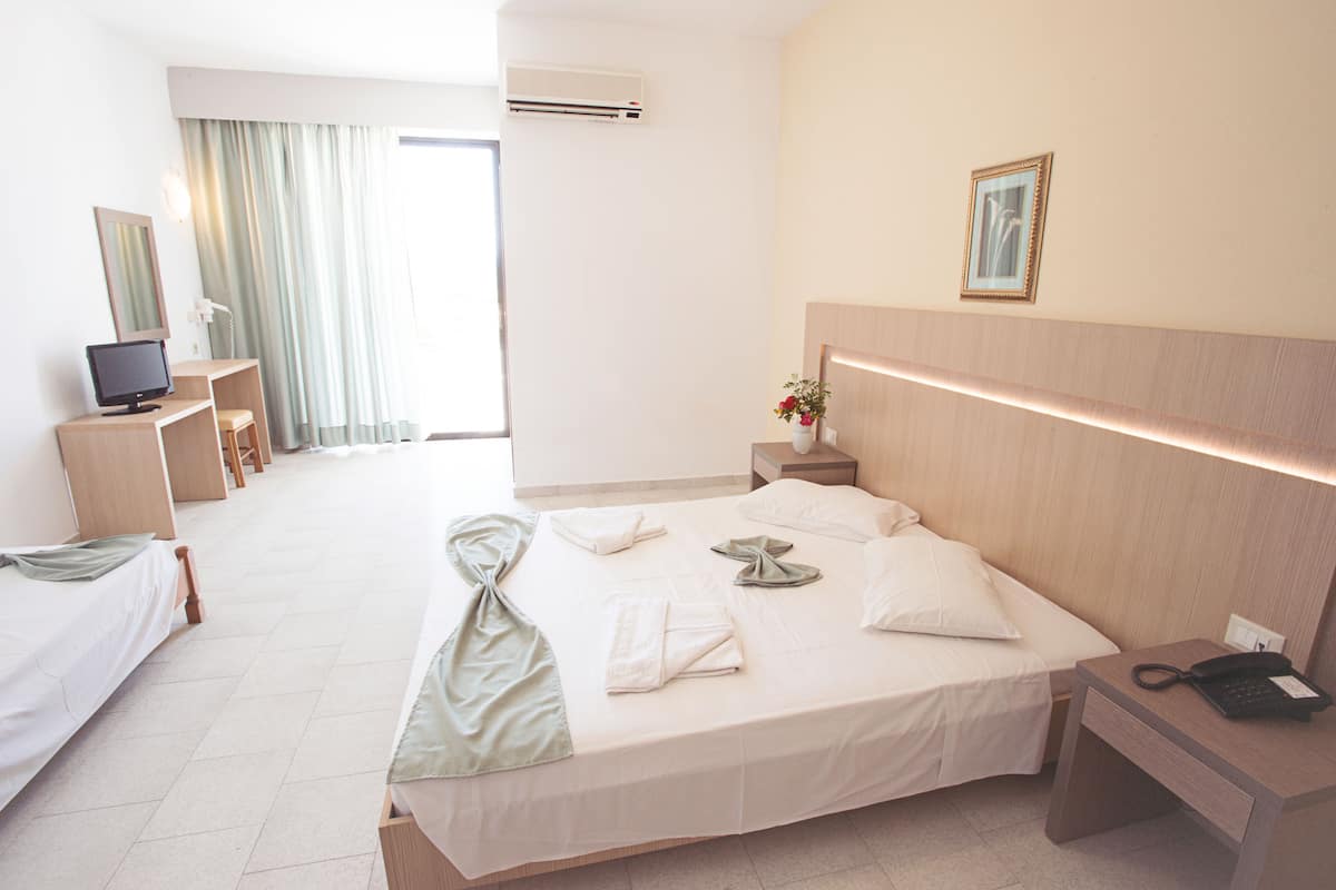 Habitación de hotel con una cama grande, un escritorio con computadora, una silla, televisor y ventana con cortinas.