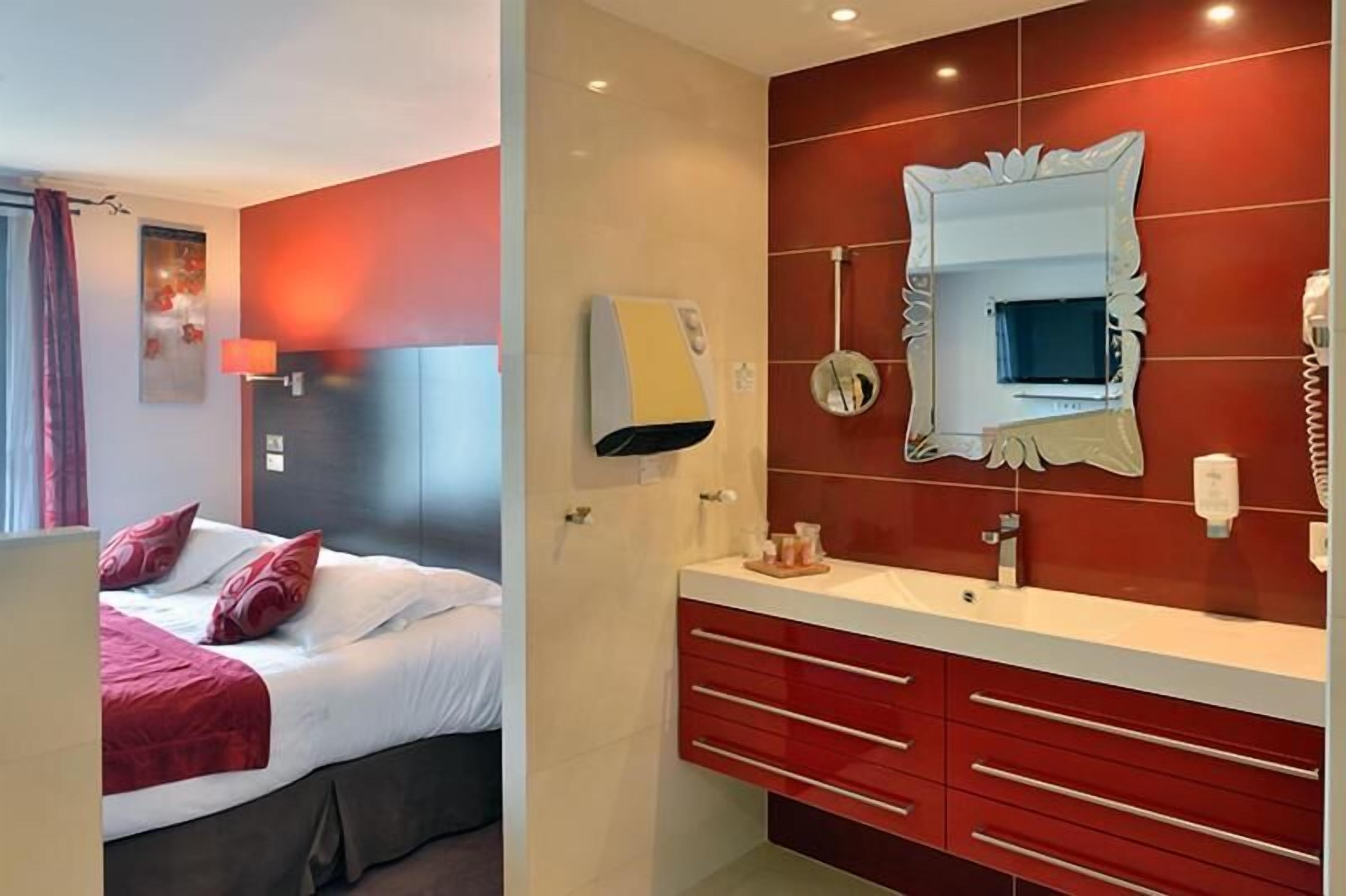 A hotel room with a bed, a vanity with a mirror, and a red wall.