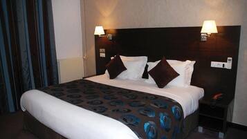 A hotel room with a large bed, two bedside lamps, a nightstand, and a window with curtains.