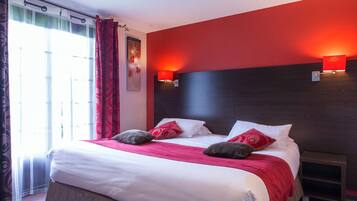 Una habitación de hotel con una cama grande, ropa de cama roja y blanca, un cabecero oscuro y una mesita de noche.