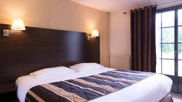 A hotel room with a large bed, two wall-mounted lamps, a window with curtains, and a radiator.