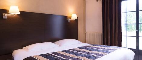 Habitación de hotel con una cama grande, dos lámparas de pared, una ventana con cortinas y un radiador.