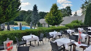 An outdoor dining area with tables and chairs, a pool in the background, and surrounding greenery. - The Originals Relais, Hôtel Restaurant Les Coquelicots (Saint-Pardoux-l'Ortigier)