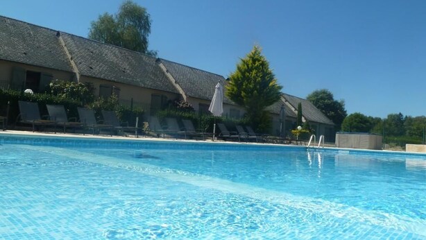 A swimming pool with clear blue water, surrounded by lounge chairs and a building with a tiled roof. - The Originals Relais, Hôtel Restaurant Les Coquelicots (Saint-Pardoux-l'Ortigier)