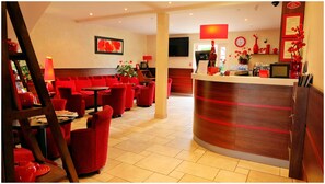 A hotel lobby with red seating, a reception desk, a television, and a clock on the wall. - The Originals Relais, Hôtel Restaurant Les Coquelicots (Saint-Pardoux-l'Ortigier)