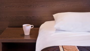 Una cama bien hecha con una almohada blanca y una taza de café sobre una mesita de noche de madera.