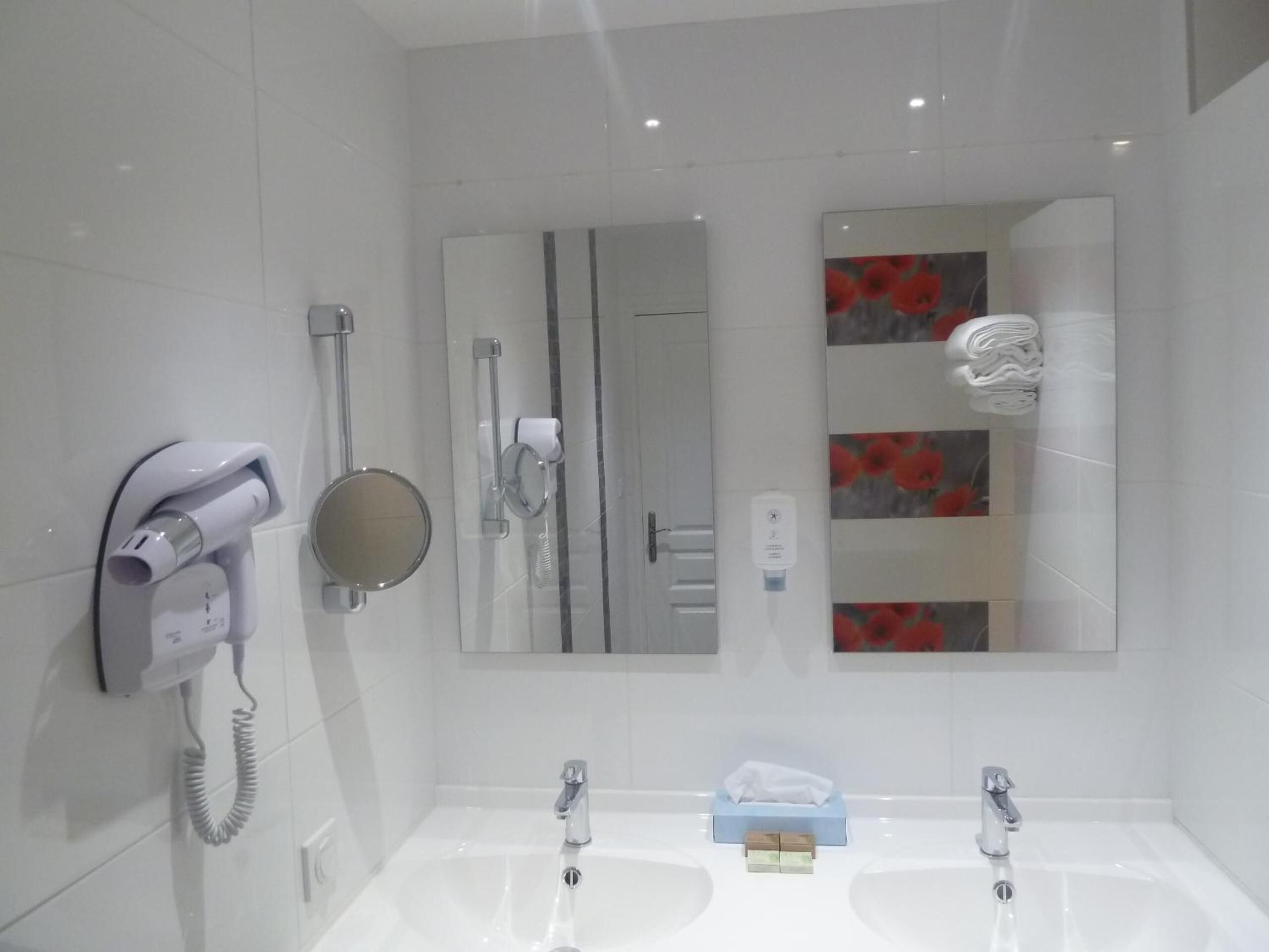 Een moderne badkamer met een haardroger, een spiegel, een handdoekrek en een wastafel met een pak tissues.