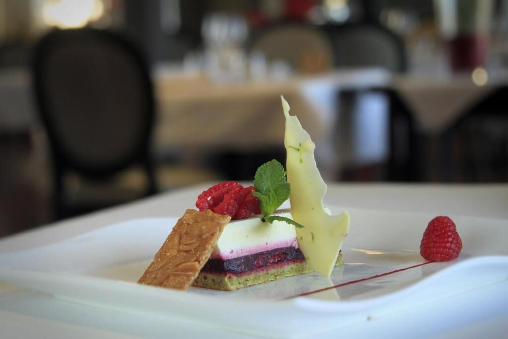 Un postre sobre un plato blanco con frambuesa, hoja de menta y un trozo de pastel.