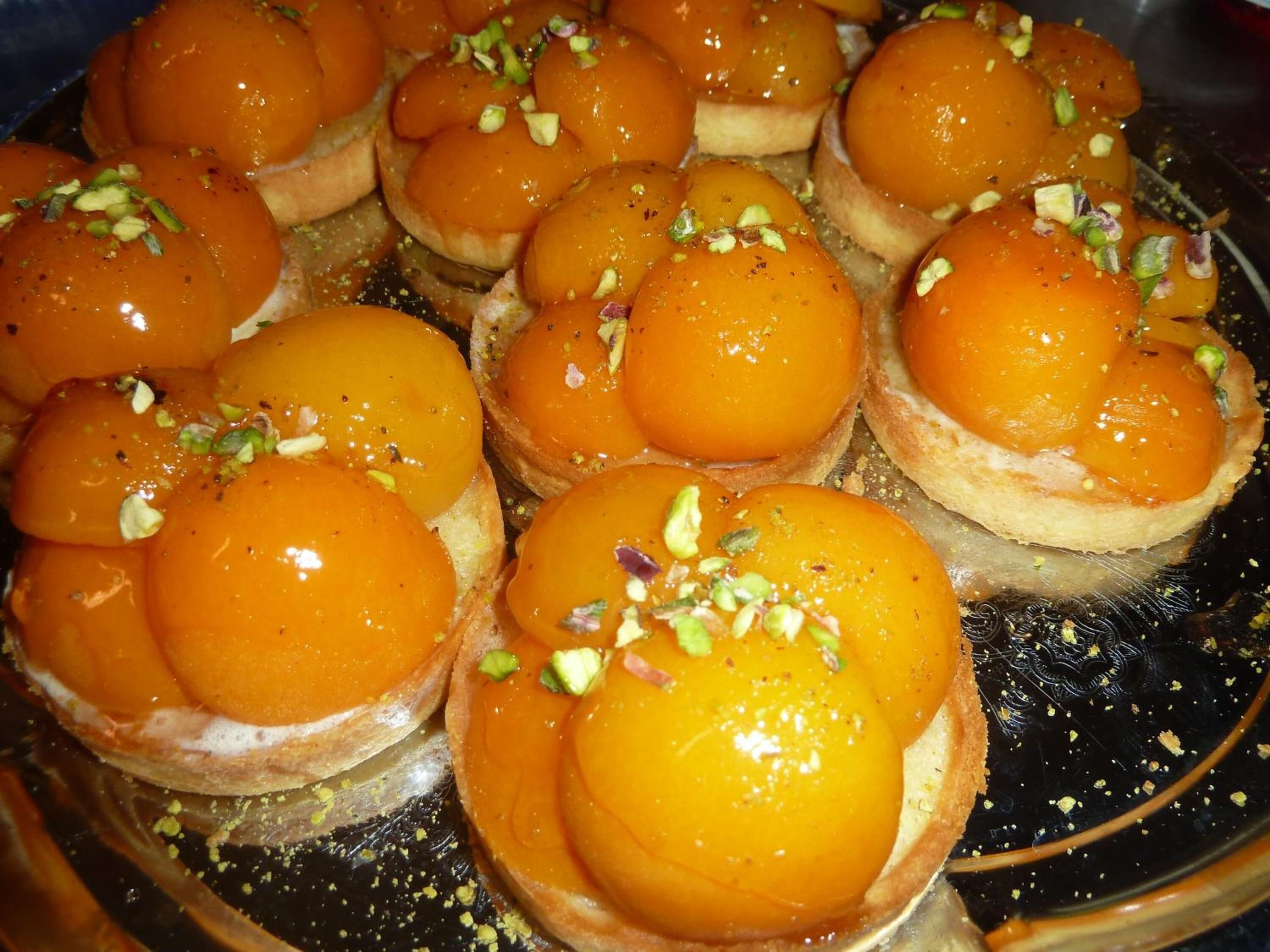 A tray of pastries topped with orange custard and garnished with chopped nuts.