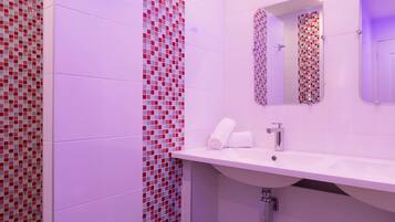 Une salle de bain avec un lavabo blanc, un miroir et un mur recouvert de carreaux rouges et gris.