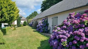 A row of traditional houses with a well-maintained lawn and purple hydrangea bushes. - The Originals Relais, Hôtel Restaurant Les Coquelicots (Saint-Pardoux-l'Ortigier)