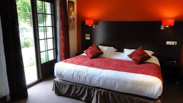 A hotel room with a large bed, red and white bedding, a view of greenery through a window, and a red accent wall.