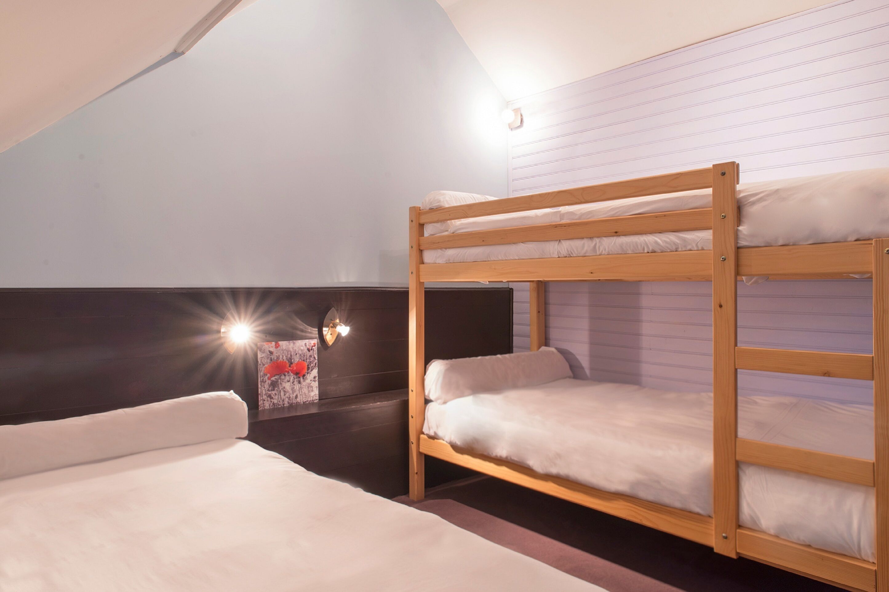 A dormitory room with bunk beds, a wall-mounted light, and a poster on the wall.