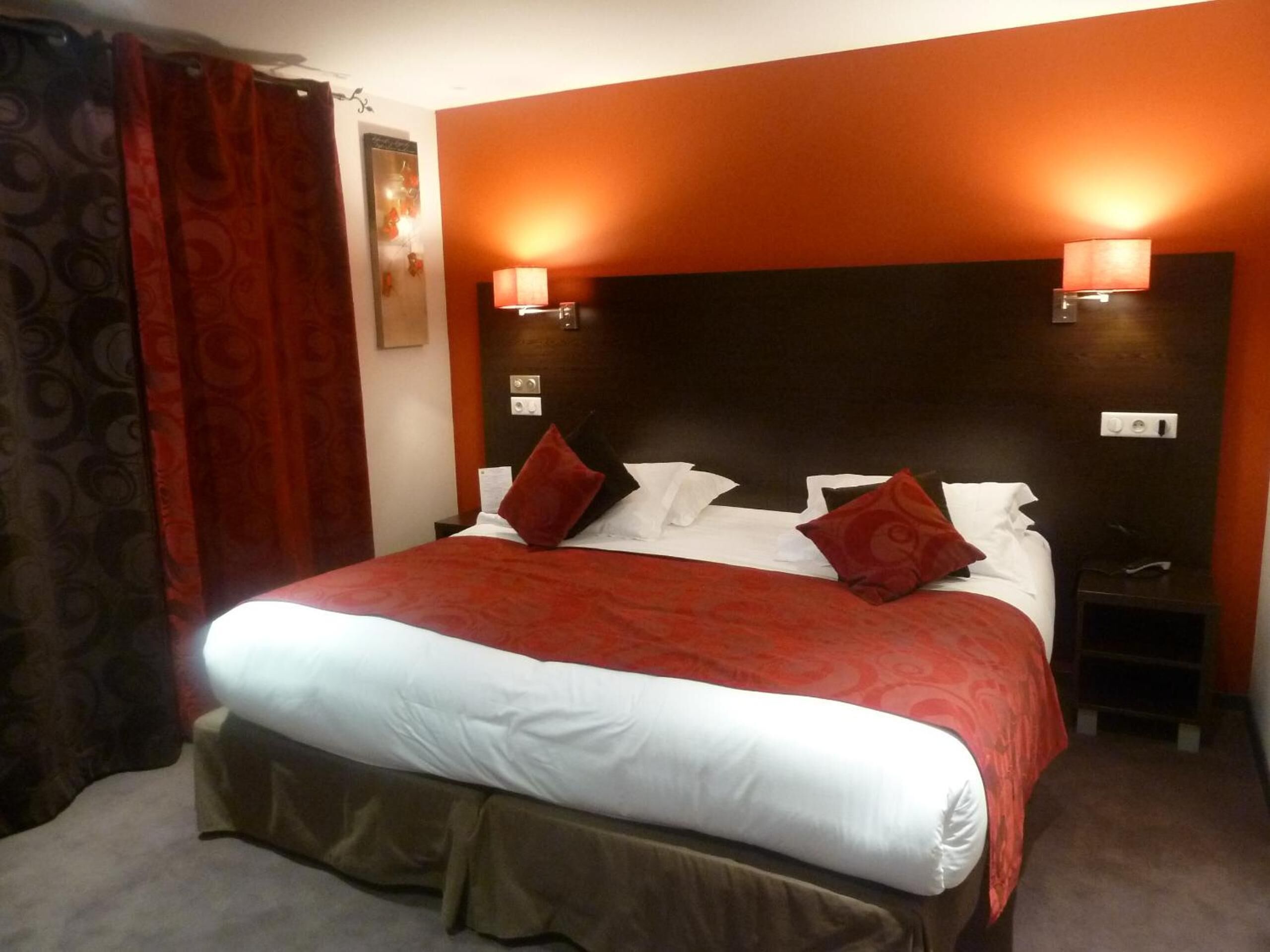 Una habitación de hotel con una cama grande, dos lámparas de noche, una mesita de noche y una cortina roja.