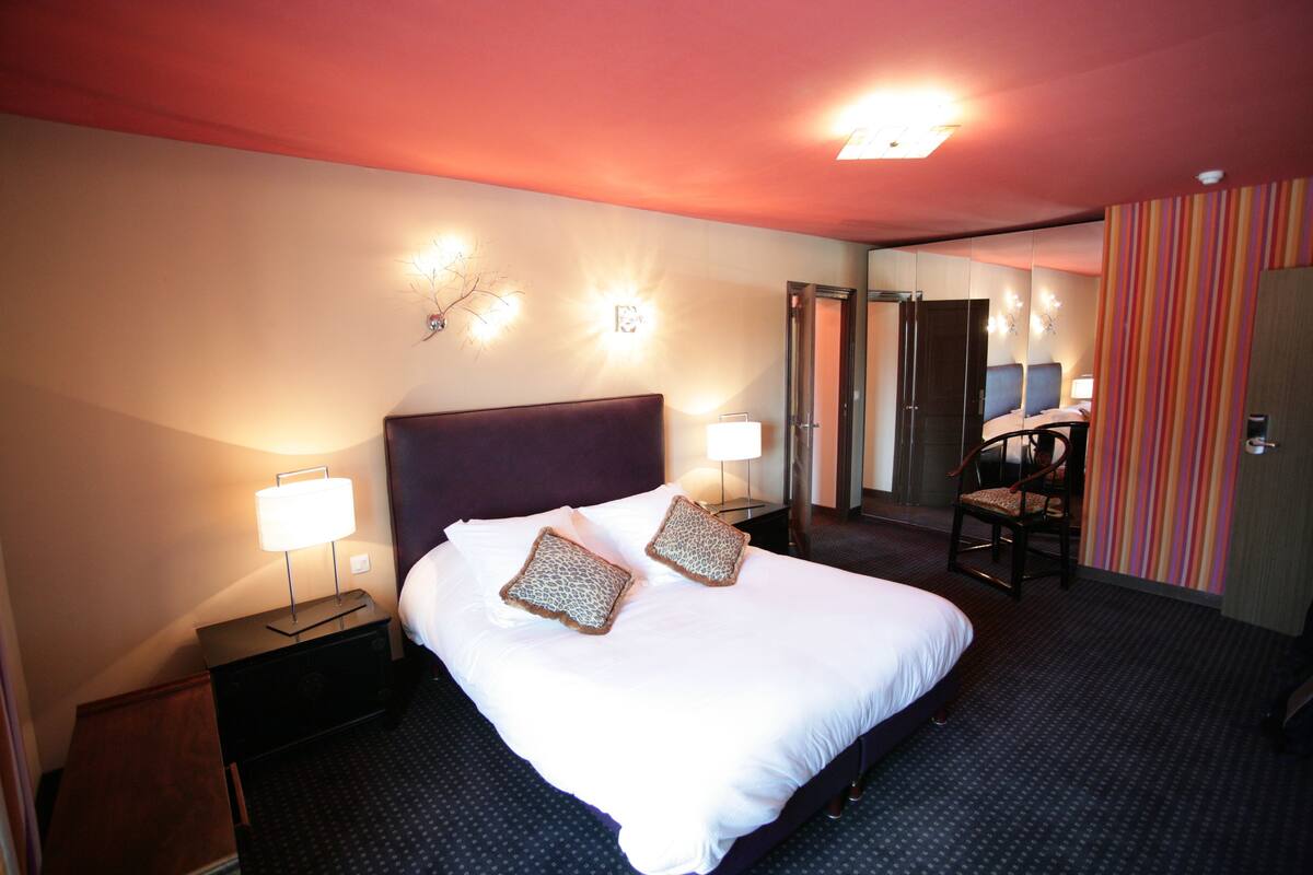 Une chambre d’hôtel avec un grand lit, deux lampes de chevet, une table de chevet, une chaise et un miroir.