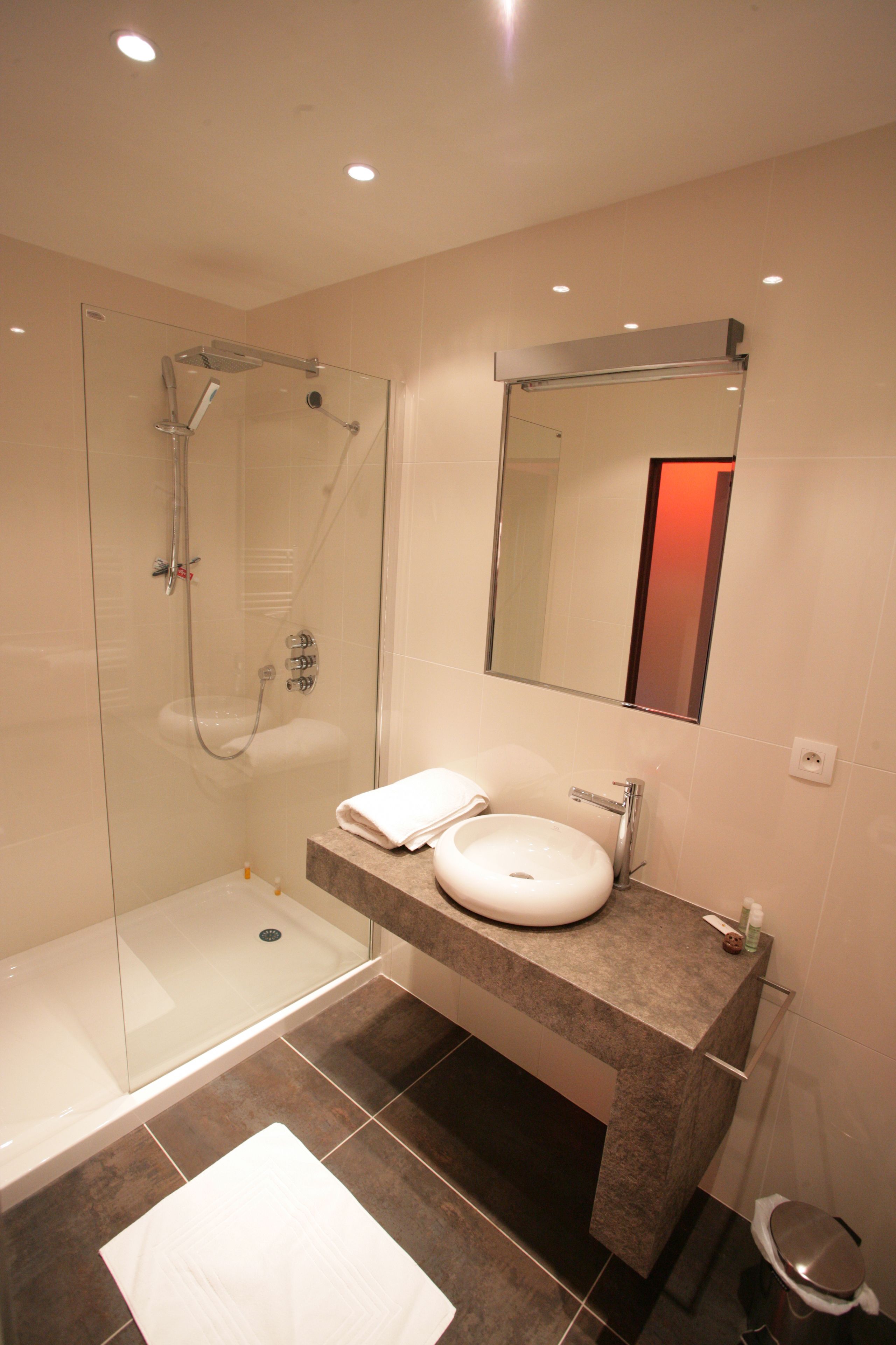 A modern bathroom with a glass-enclosed shower, a white sink, and a large mirror.