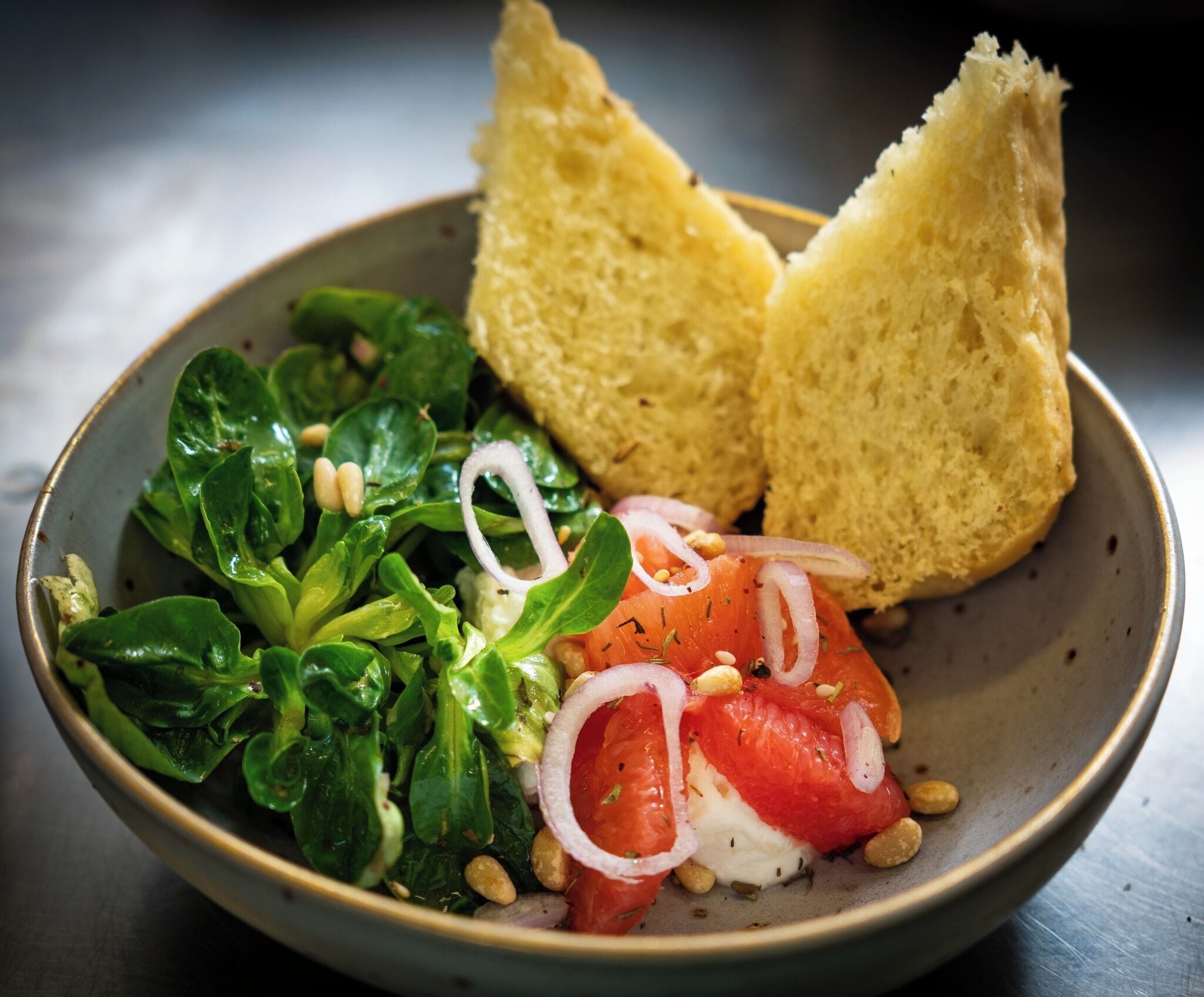 Un tazón de ensalada con espinacas, tomates y cebollas, acompañado de dos rebanadas de pan.