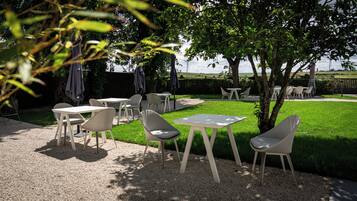 An outdoor seating area with tables and chairs, surrounded by greenery and a view of the landscape.