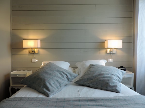 Una habitación de hotel con una cama, dos mesitas de noche y lámparas fijadas a la pared.