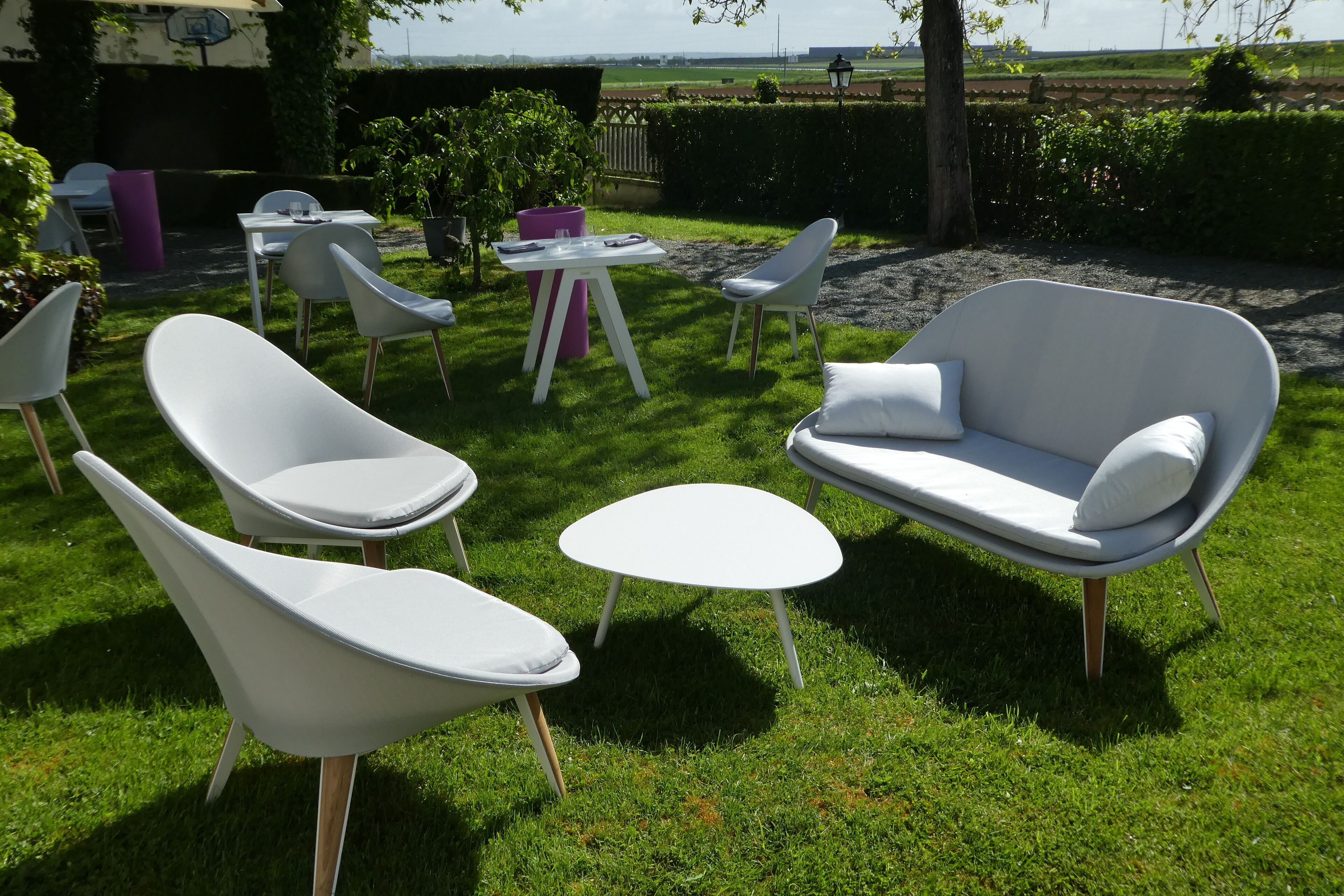 An outdoor seating area with modern white chairs and a sofa, a small round table, and a purple trash bin.