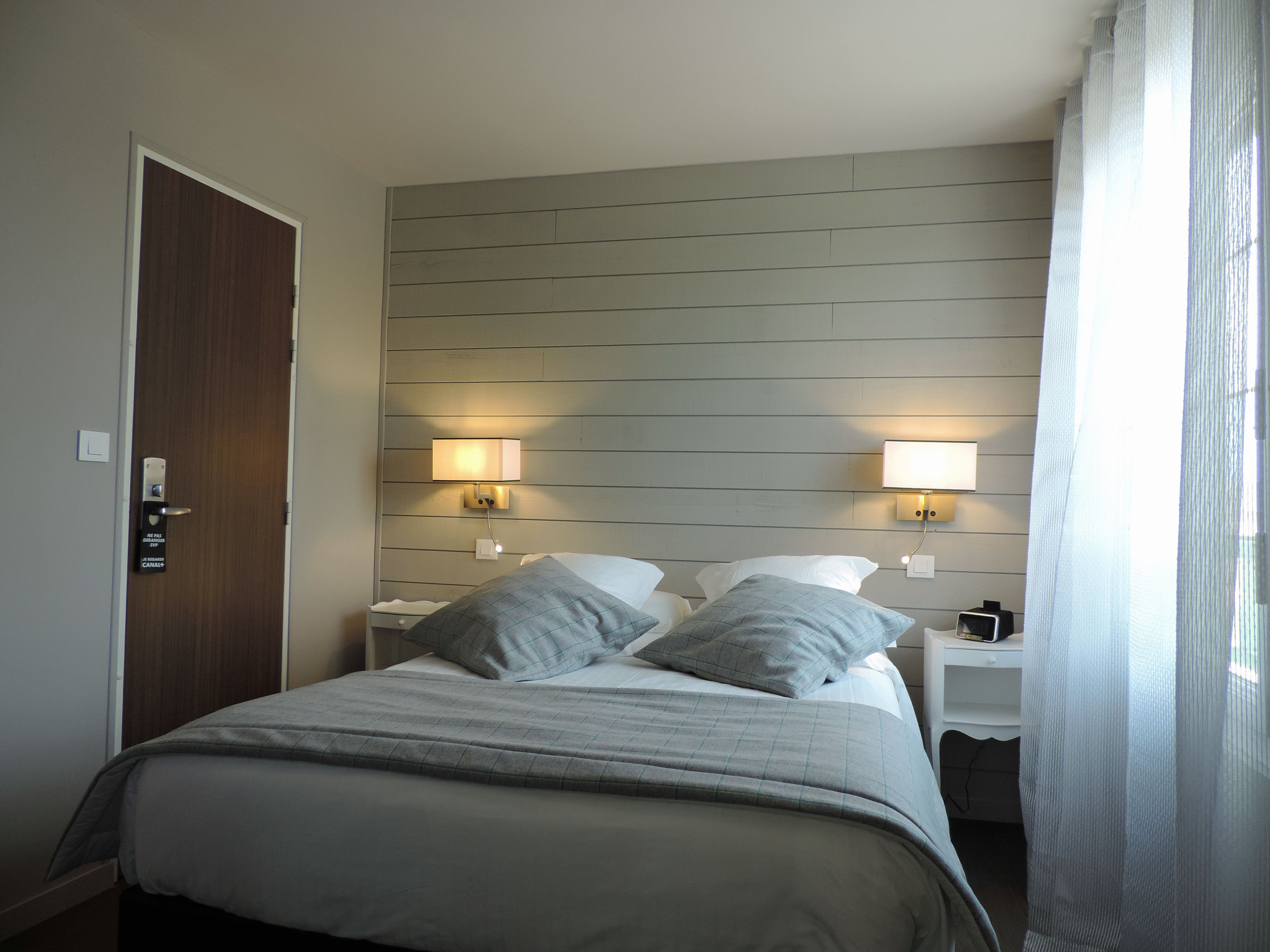 Habitación de hotel con cama, dos mesitas de noche, una lámpara de pared y una puerta.