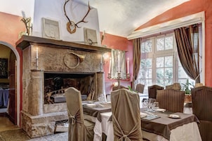 Uma sala de jantar com lareira de pedra, cadeiras de madeira e uma mesa posta para refeição.