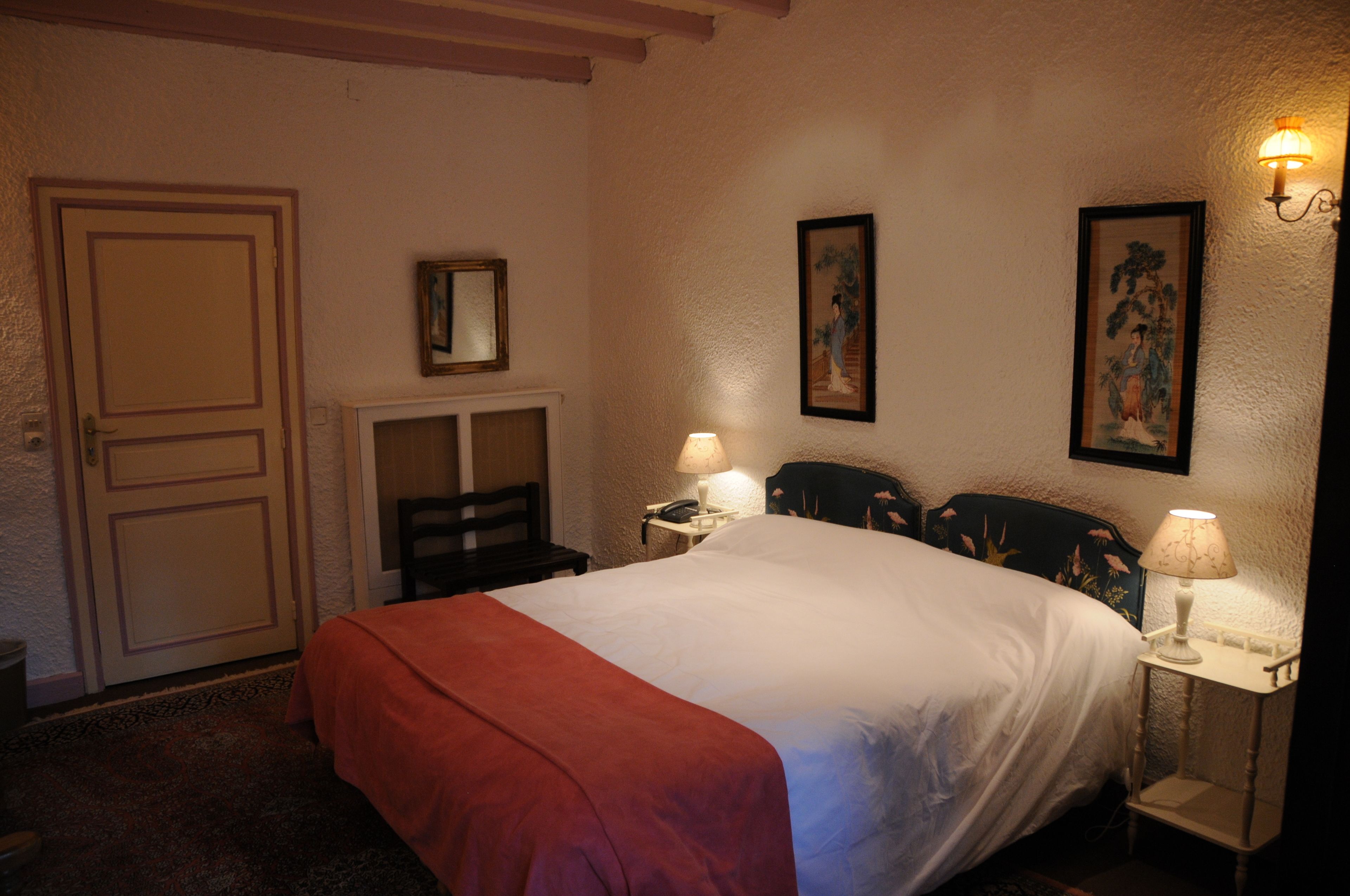 A bedroom with a bed, two bedside tables with lamps, a chair, a door, and two framed pictures on the wall.