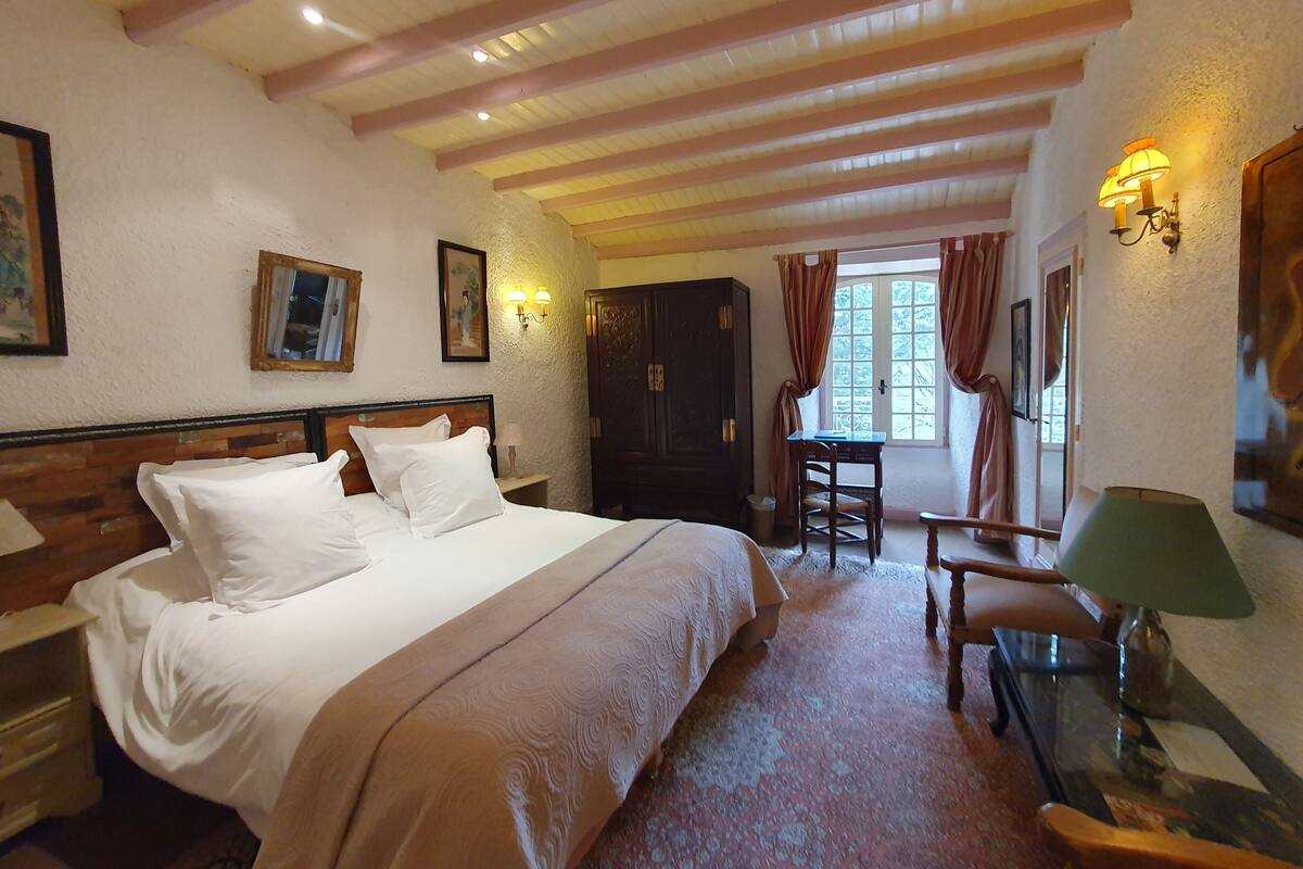 A hotel room with a large bed, a desk, a chair, and a lamp.
