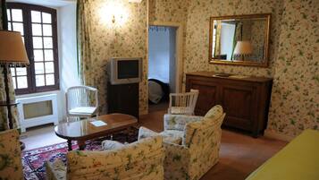 A room with floral wallpaper, a wooden cabinet, a television, a mirror, and a window with curtains.