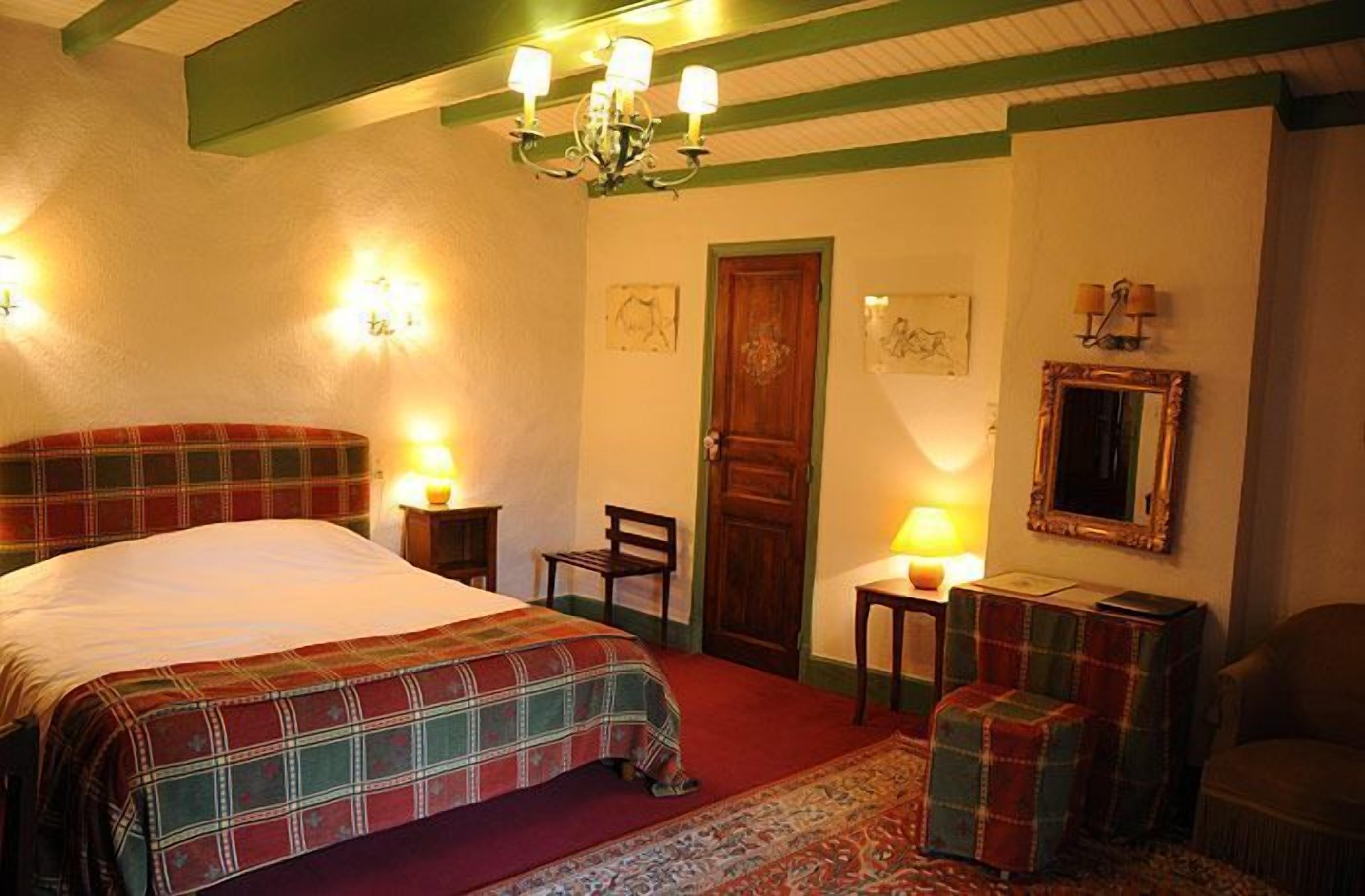 Una habitación acogedora con una cama grande, una puerta de madera, un espejo y una pequeña mesa con una lámpara.