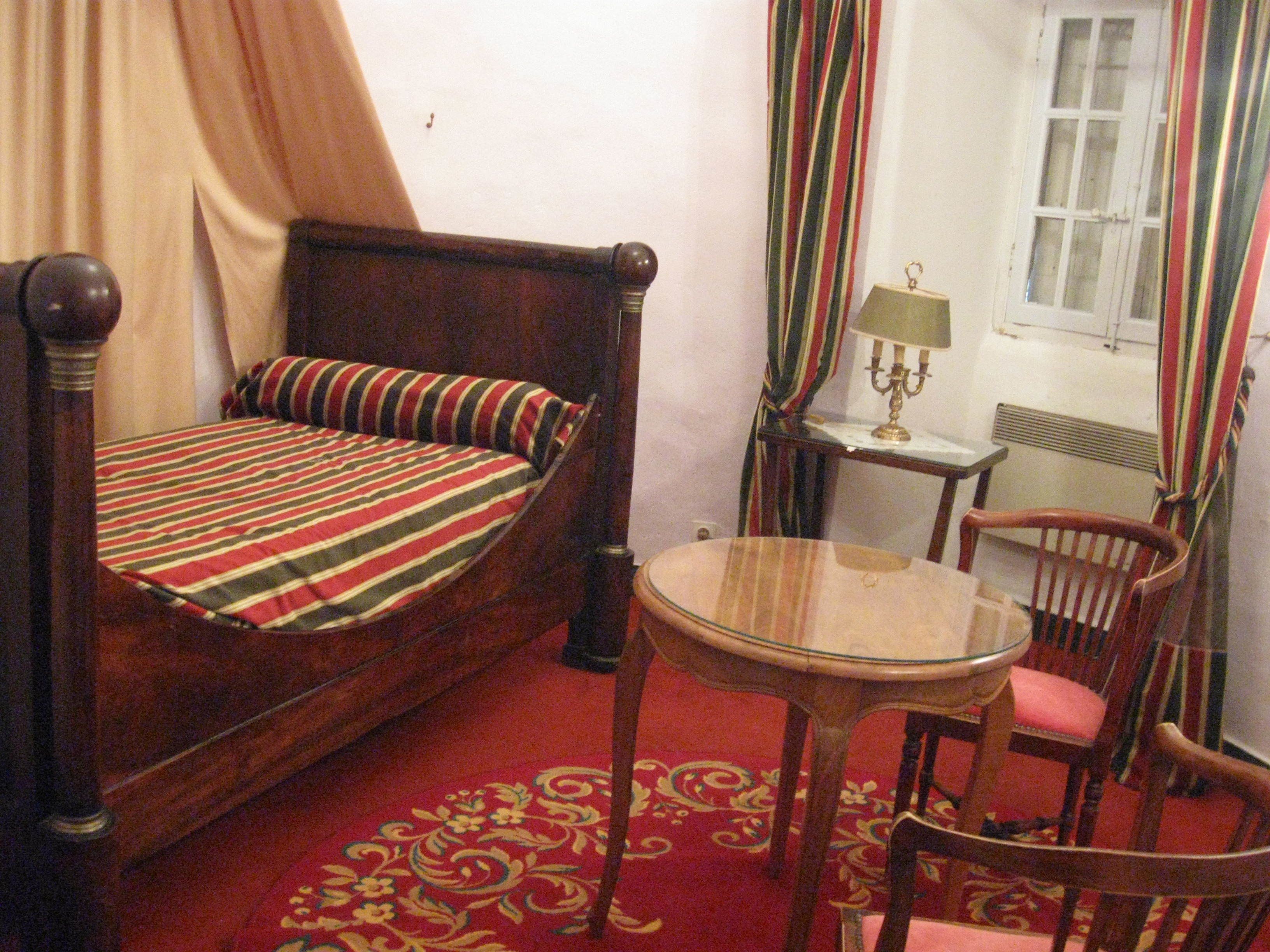 A room with a bed, a small round table, a chair, a lamp, and a window with curtains.