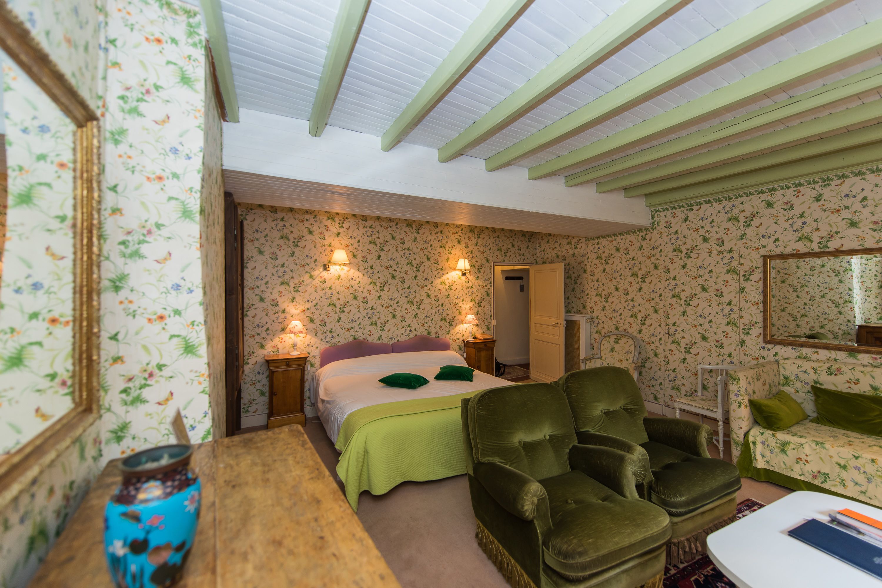 Una habitación con una cama, dos mesitas de noche, un sillón verde, un sofá blanco y un espejo en la pared.
