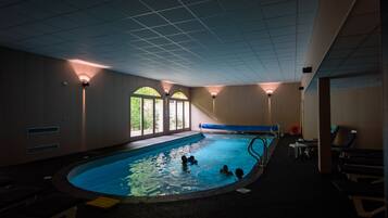 An indoor swimming pool with a tiled ceiling, windows, and a few people swimming.