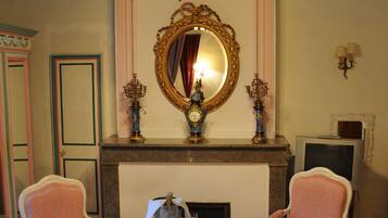 A room with a fireplace, two chairs, a small table, a mirror, and a television.