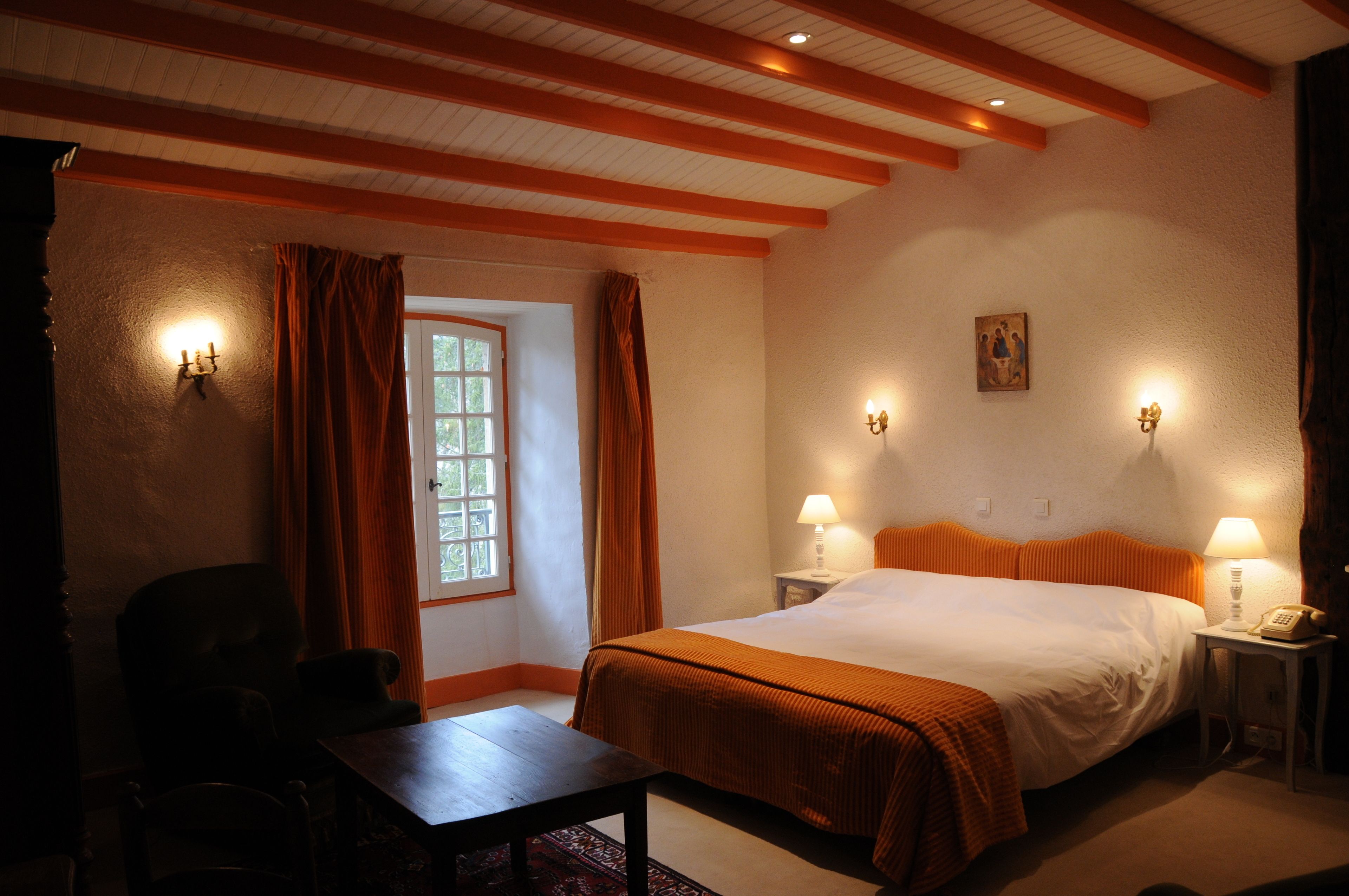 A hotel room with a large bed, two bedside tables with lamps, a window with curtains, and a wooden table.