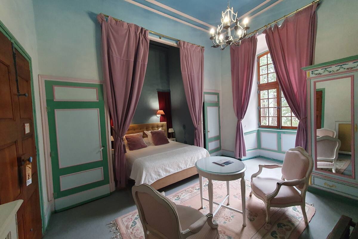 A bedroom with a bed, a chair, a table, and a chandelier.