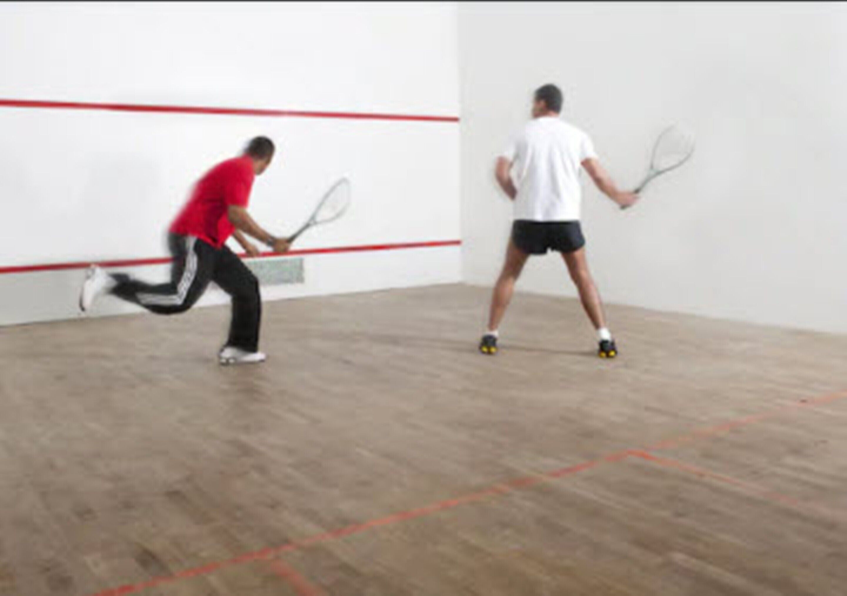 A squash court with wooden flooring and red boundary lines.