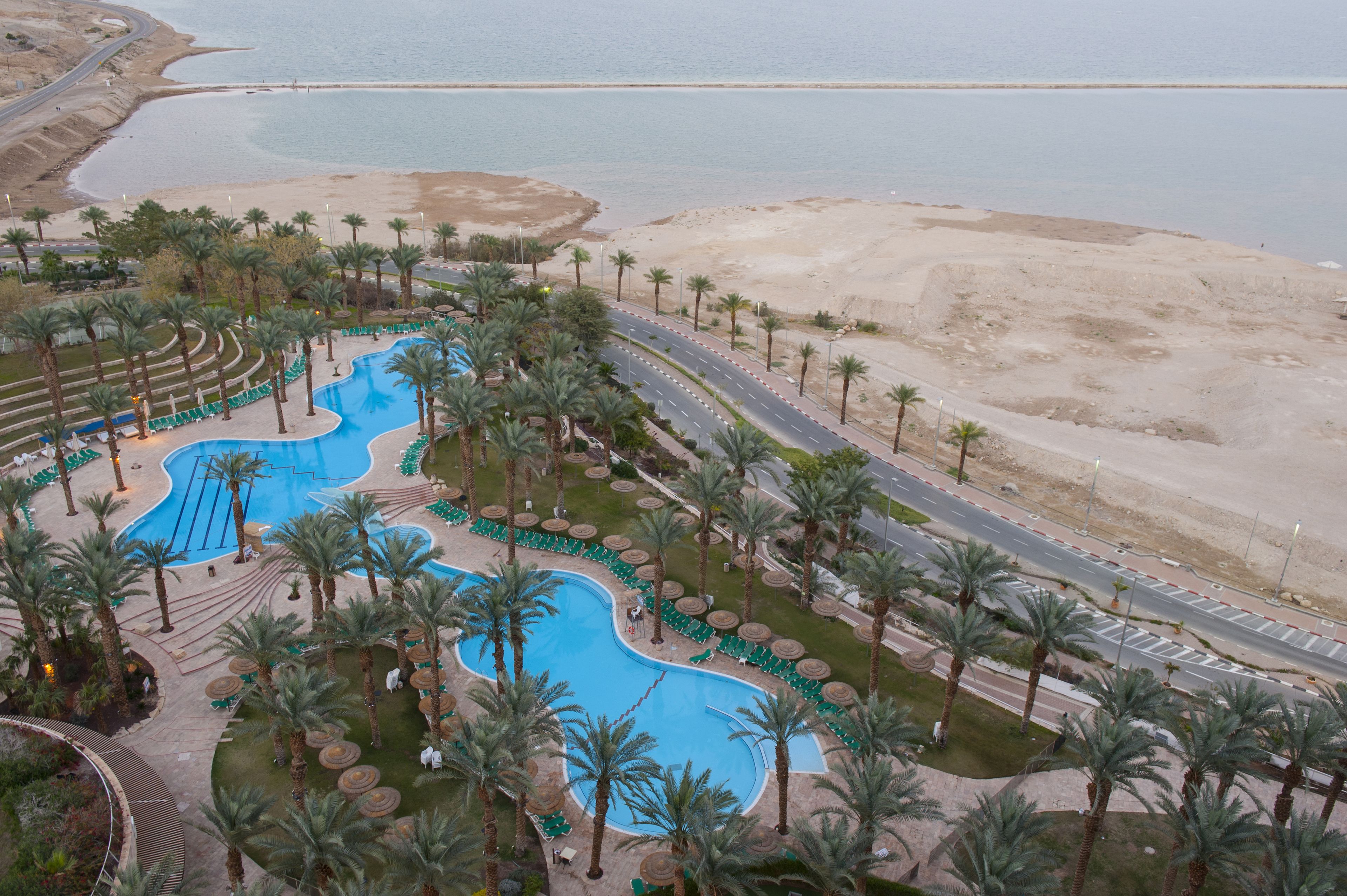 Et resort med en stor swimmingpool, palmer og en vej der fører til stranden.