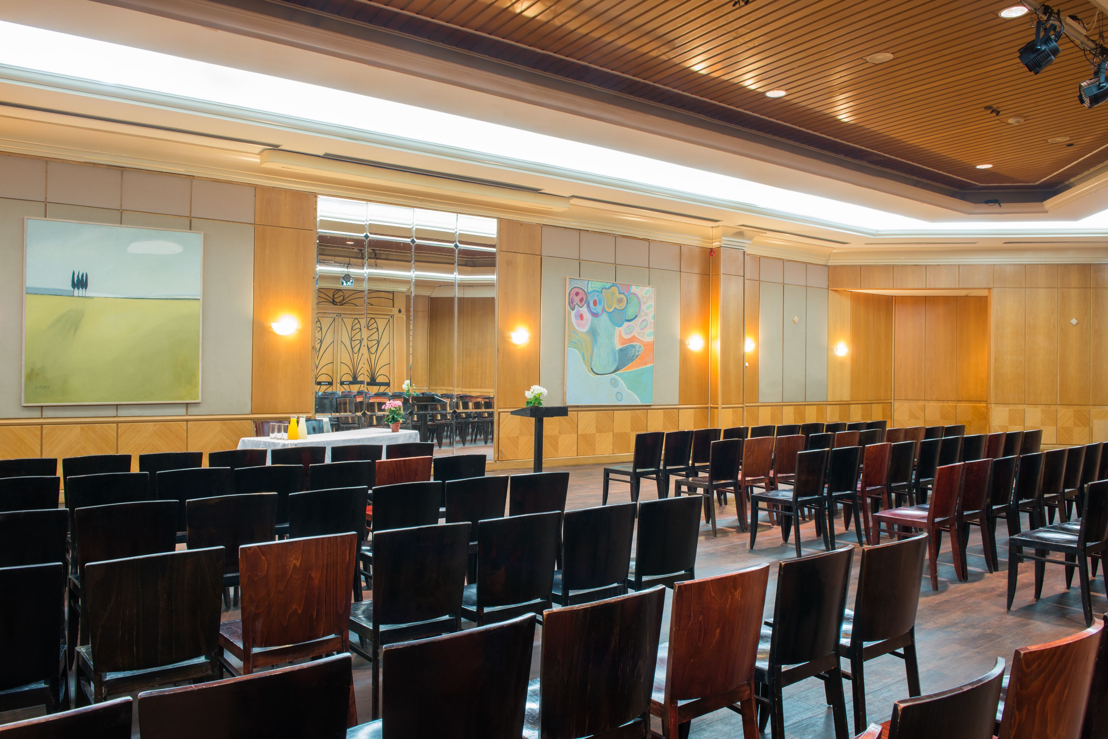 Un salón de conferencias con filas de sillas, un escenario y obras de arte en las paredes.