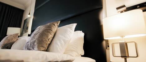 A neatly made bed with white linens and multiple pillows, a modern bedside lamp, and a dark headboard.