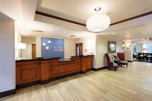 A hotel reception area with a wooden reception desk, a blue wall with the hotel name, a large chandelier, and a seating area with chairs. - Holiday Inn Exp Walterboro by IHG (Walterboro)