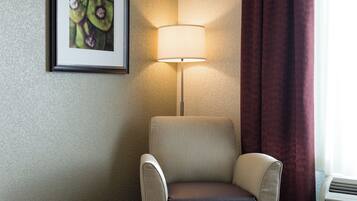 A hotel room with a single armchair, a wall-mounted lamp, and a framed picture.