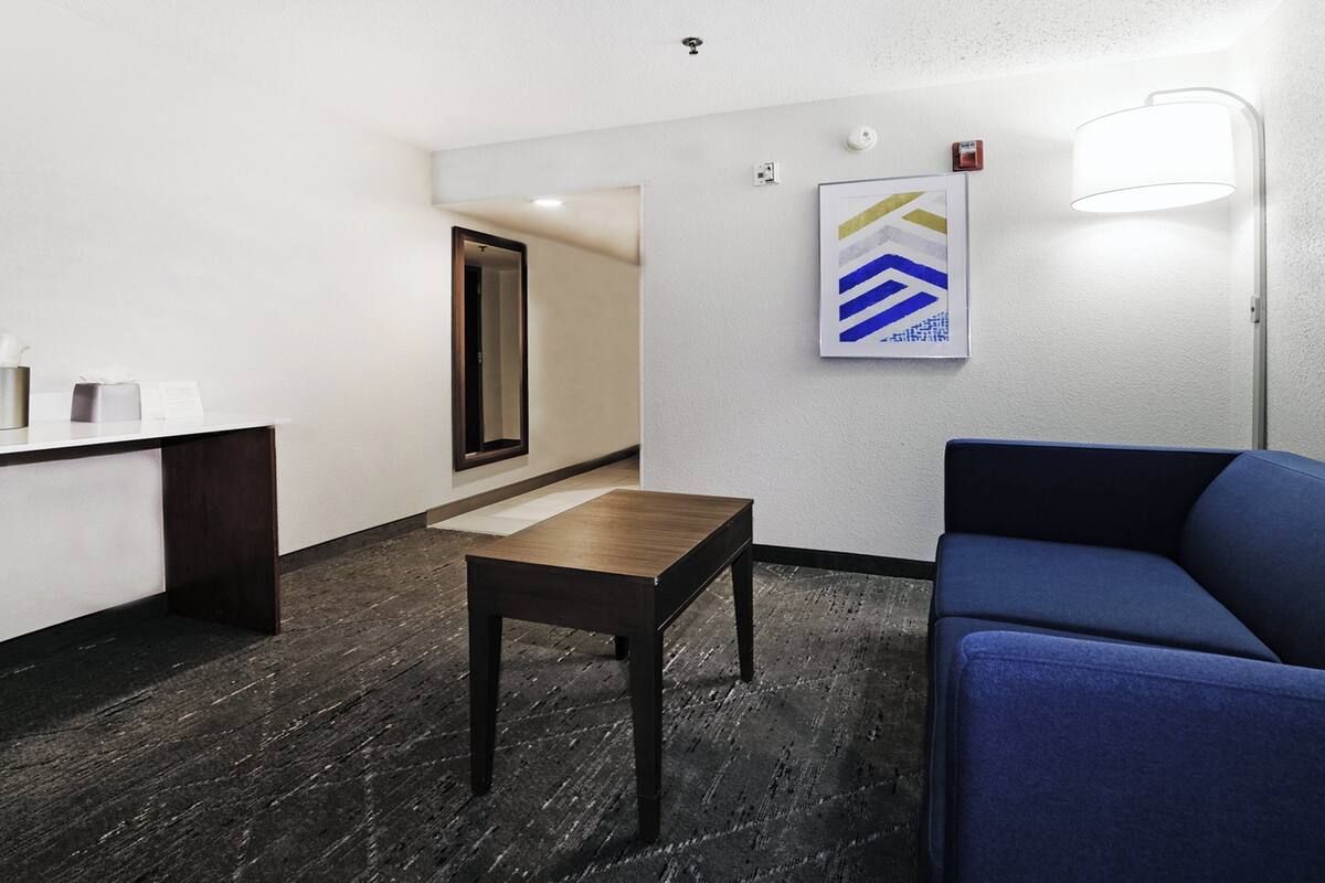 A hotel lobby with a reception desk, a blue sofa, a small table, and a framed artwork on the wall.