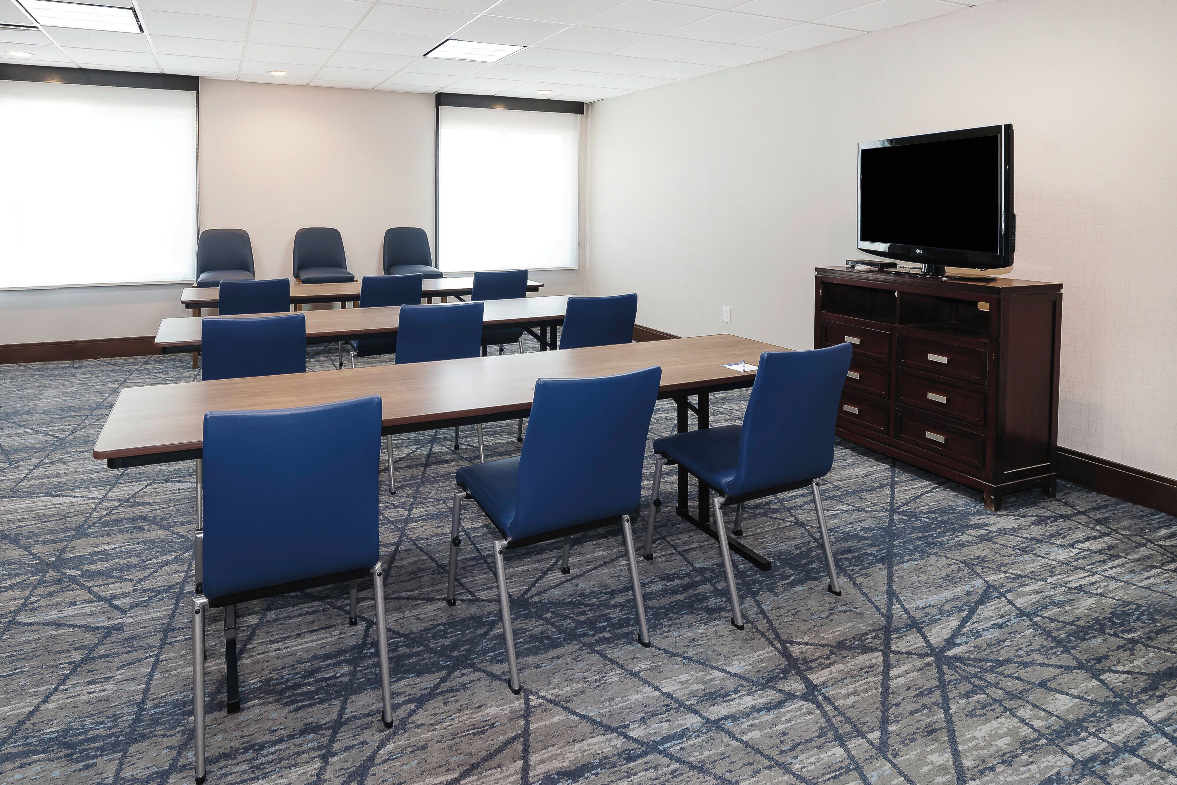 A conference room with a large table, blue chairs, a television on a cabinet, and a patterned carpet.