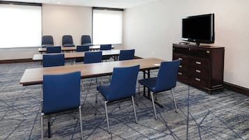 A conference room with a large table, blue chairs, a television on a cabinet, and a patterned carpet.
