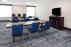 A conference room with a large table, blue chairs, a television on a cabinet, and a patterned carpet.